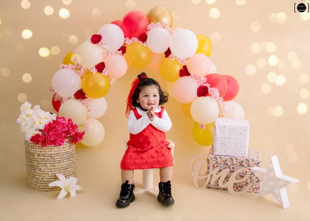 Baby photoshoot preview — a smiling baby girl at a first-birthday balloon setup in South Delhi studio by Priyansh Bhardwaj.